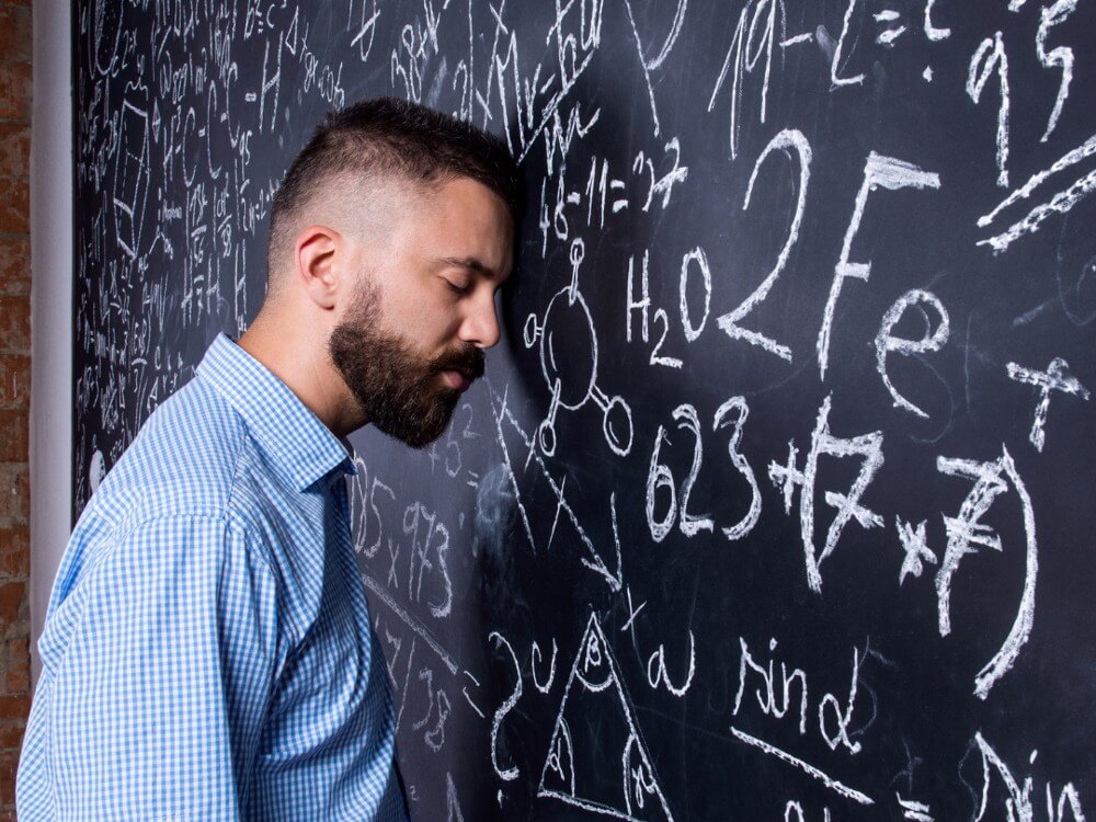 A burned out teacher leans his head against the blackboard, thinking 