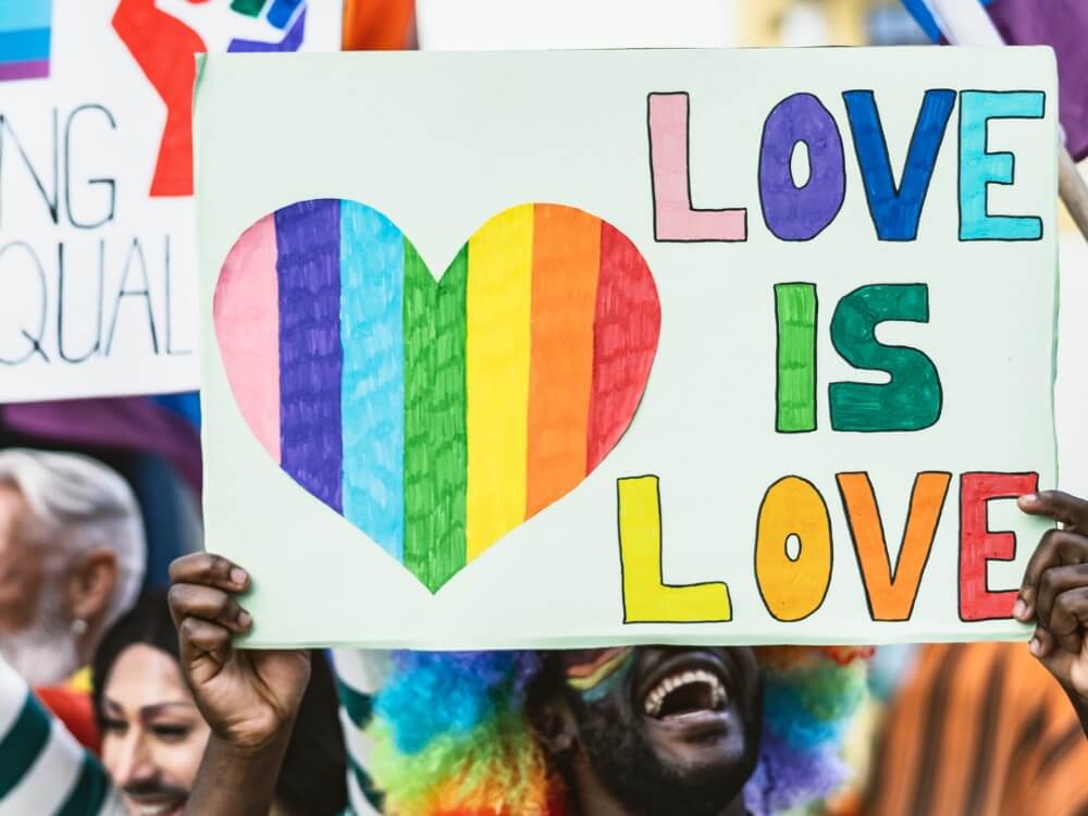 Man in rainbow wig holding sign that says love is love.