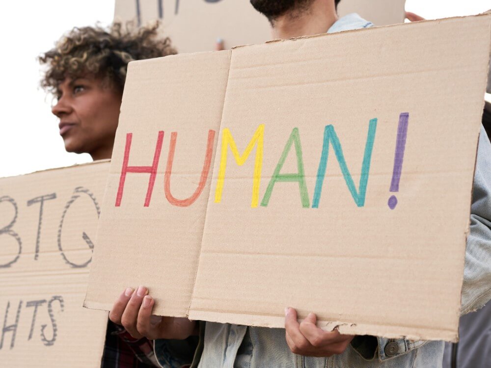 Man holding cardboard sign with the word human written in rainbow letters.