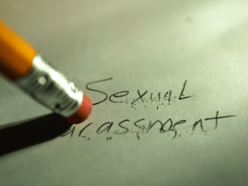The words "sexual harassment" written in pencil on paper being erased.