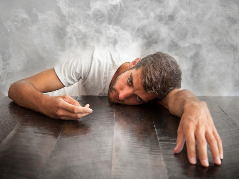 Man laying on table with lower half of his body in smoke.