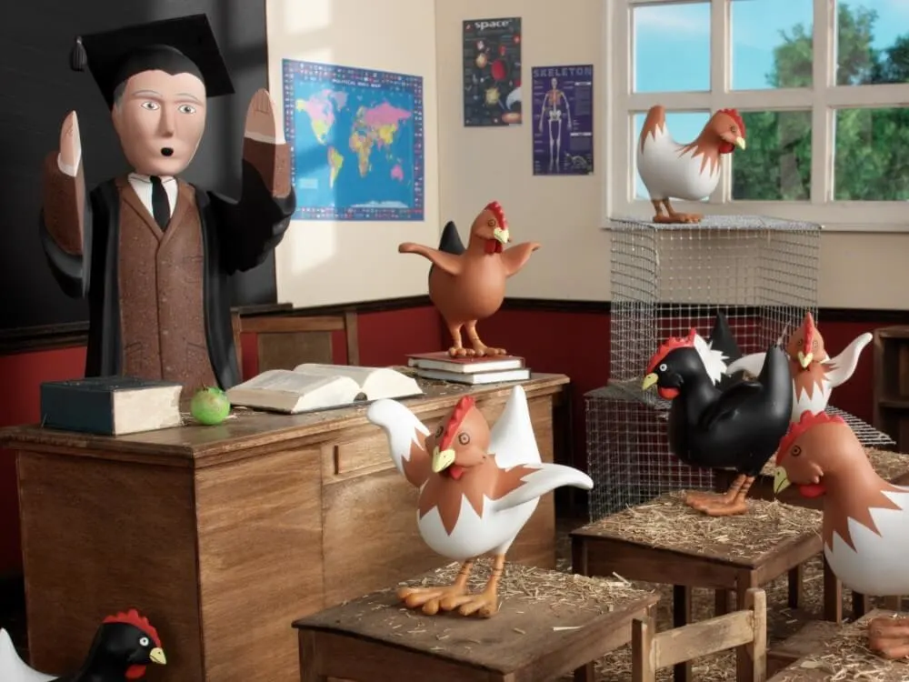 Wooden figurines of a teacher in a classroom surrounded by chickens.