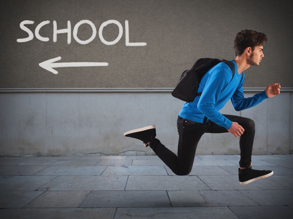 Boy with backpack running away from a sign that says, "school."