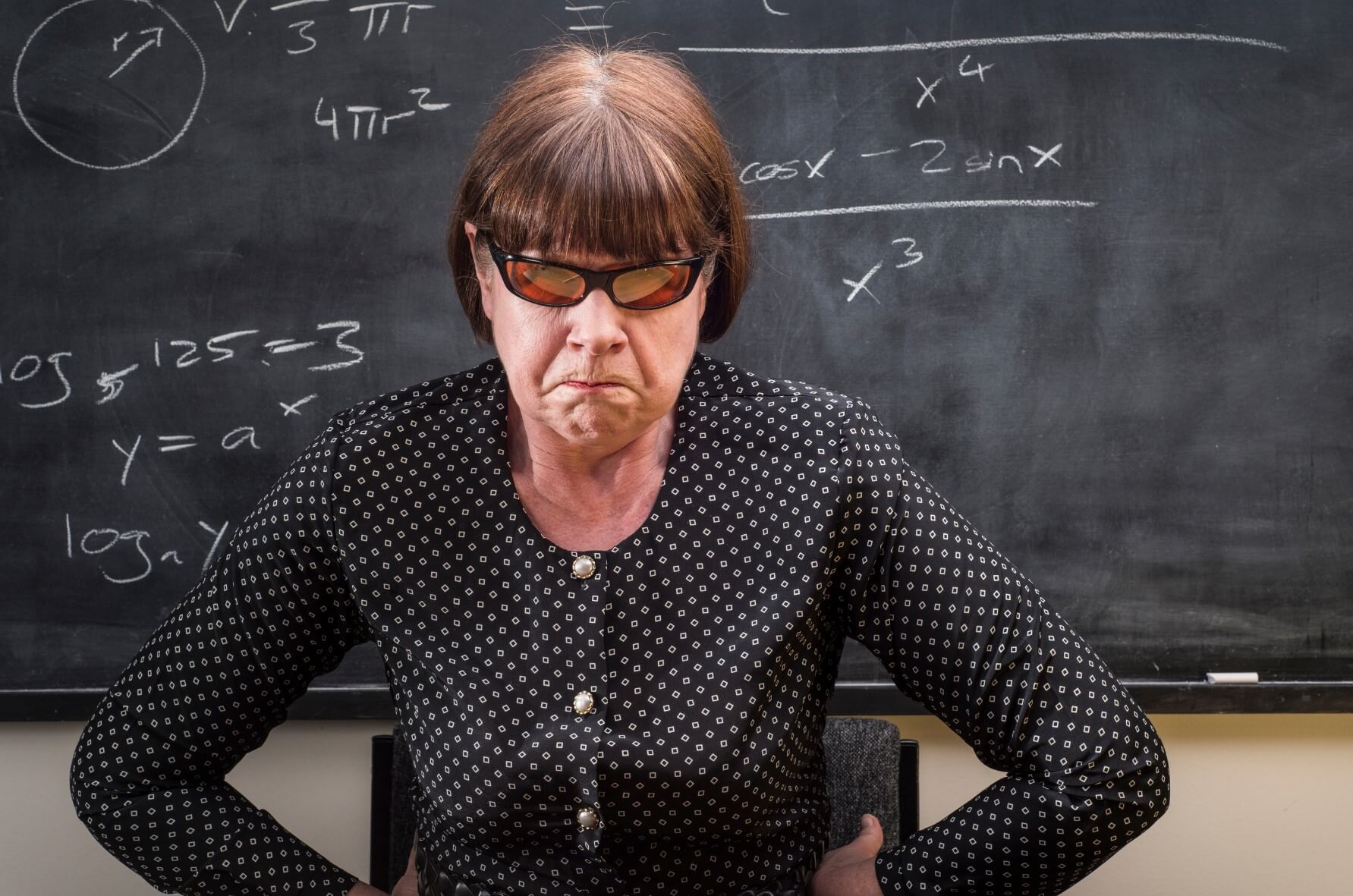 An angry veteran teacher in front of a blackboard demonstrates to a new class the tone they can expect for the school year.