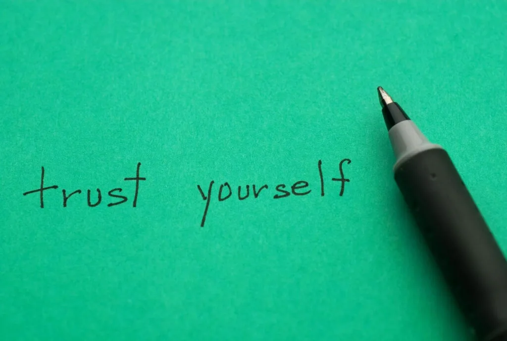A pen and green paper with the words "Trust Yourself" written on it, representing the self-prioritization needed if you are a bullied teacher.