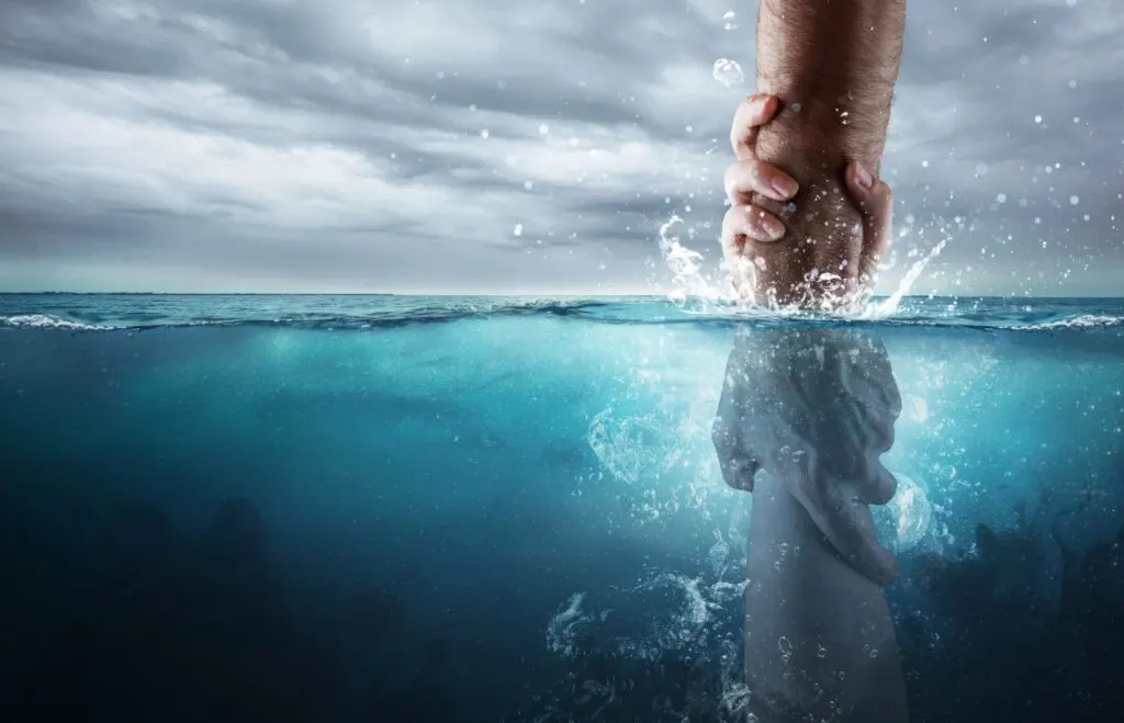 A hand pulling another hand out of the water representing the feeling of drowning when suffering from workplace bullying.