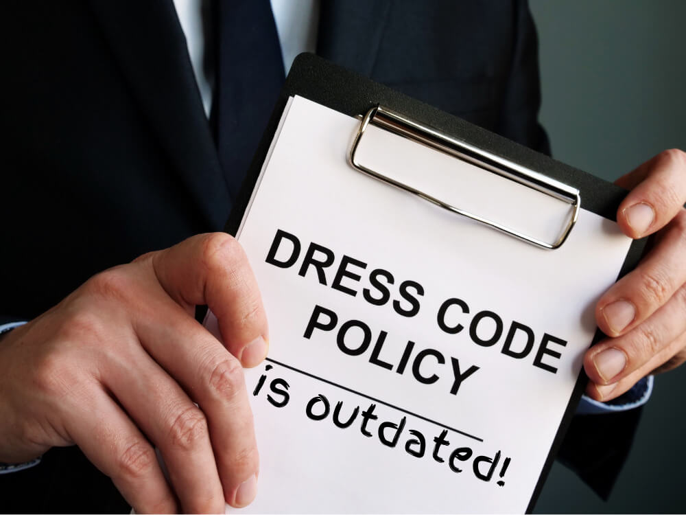 The words "Dress Code Policy" on a clipboard with "is outdated!" scribbled beneath.