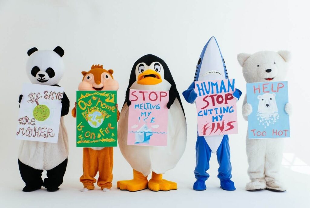 A line of people in different animal costumes holding signs promoting environmental awareness.