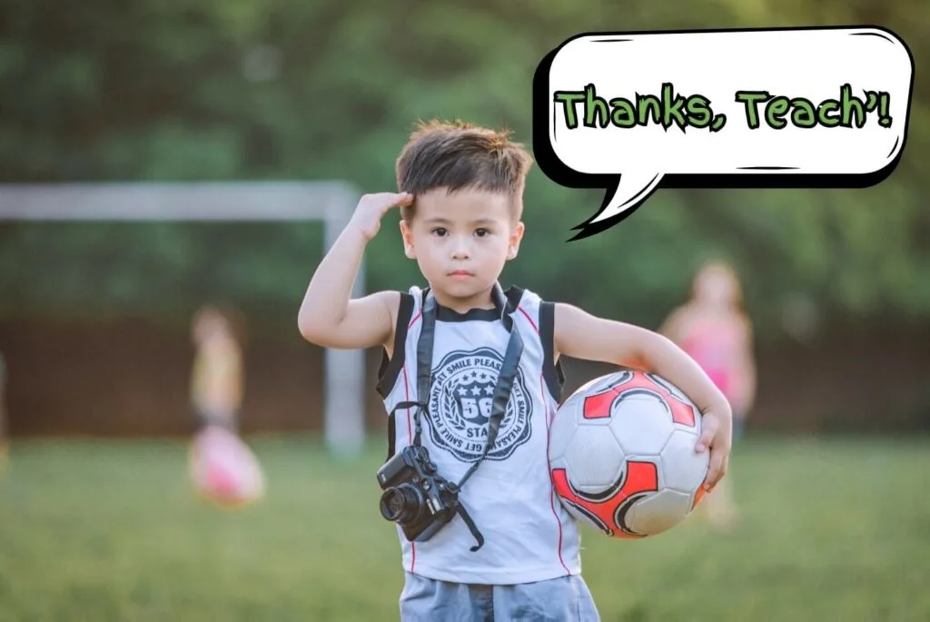 A young boy on a soccer field holding a soccer ball and saluting the camera to thank his teacher.