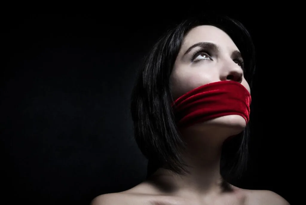 A teacher with a red cloth tied over her mouth, representing the experience of being silenced as a victim of sexual harassment.